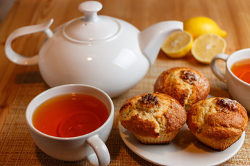 teapot is white and two white cups of tea with lemon and muffins