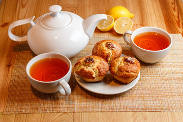 teapot is white and two white cups of tea with lemon and muffins