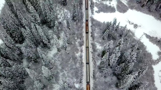 Camera slowly tilts up over a freight train travelling through a winter landscape. Aerial view