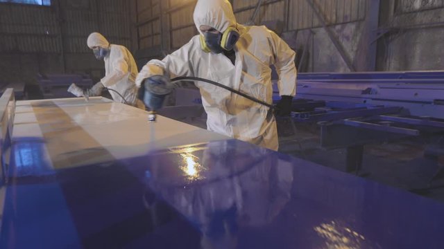 Men paint a large detail in blue, Painting at the factory. Painting large parts