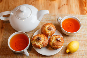 teapot is white and two white cups of tea with lemon and muffins