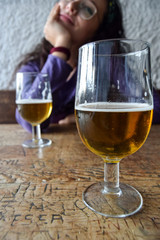 close-up of a glass of beer with a young woman in the background having beers in the afternoon in a bar inside a cave in autumn