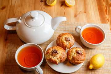 teapot is white and two white cups of tea with lemon and muffins