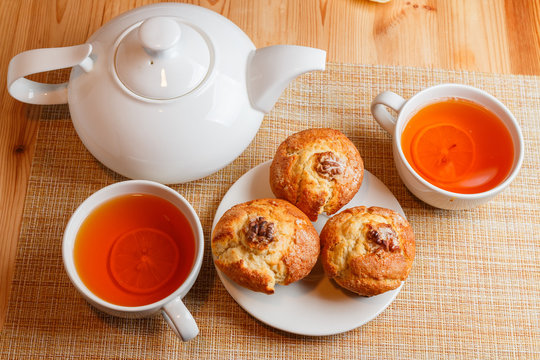 teapot is white and two white cups of tea with lemon and muffins