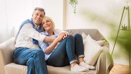 Love lives forever! Loving senior couple embracing, sitting on sofa