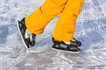 Legs of teenager boy in bright yellow clothe in ice skates, closeup skating shoes in winter, healthy lifestyle.