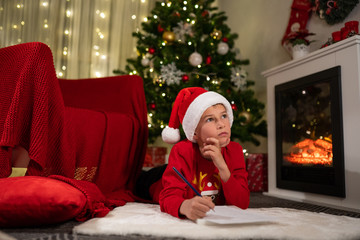 the boy lies under the Christmas tree near the fireplace and writes a letter to Santa Claus