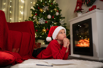 the boy lies under the Christmas tree near the fireplace and writes a letter to Santa Claus