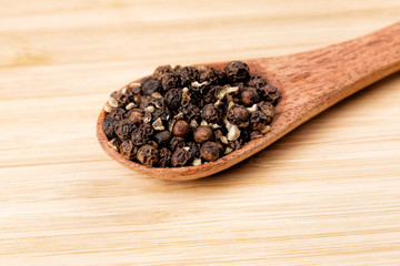 Spoon full of black peppercorns on a wooden background