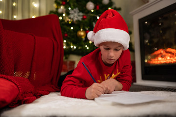 the boy lies under the Christmas tree near the fireplace and writes a letter to Santa Claus