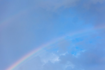 A piece of rainbow in the sky against the background of rain clouds.