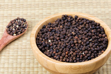 Bowl full of black peppercorns on a bamboo background