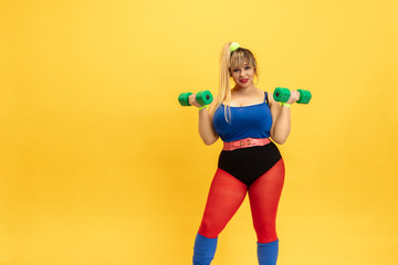 Fototapeta na wymiar Young caucasian plus size female model's training on yellow background. Stylish woman in bright clothes. Copyspace. Concept of sport, healthy lifestyle, body positive, fashion. Practicing with weights
