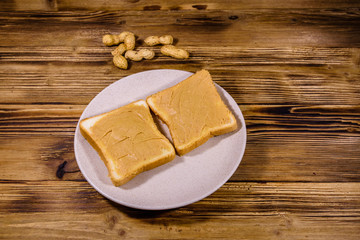 Glass jar with peanut butter and plate with sandwiches on a wooden table