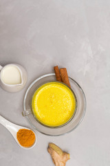 Obraz na płótnie Canvas Traditional Indian drink Turmeric Golden Milk in a glass cup with ingredients cinnamon sticks, turmeric powder, ginger root and milk on grey concrete table