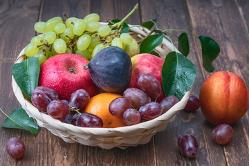 red and white grapes and fresh fruits in a straw basket on a dark wooden background
