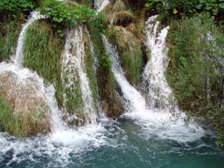 Top view of falling water into a crystal clear lake on a mountain slope richly covered with tall grass.