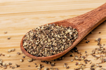 Spoon full of ground black pepper on a wooden background