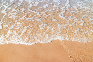 Fototapeta na wymiar Shallow water on the shore as gentle waves break over warm yellow sand at the beach