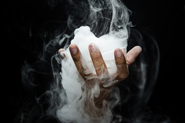Hand smoke from dry ice in a bowl, black background. - obrazy, fototapety, plakaty