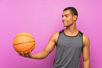Young sport man with ball of basketball over isolated purple wall with happy expression