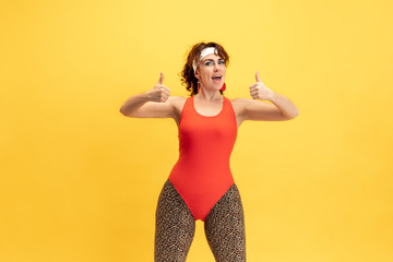 Young caucasian plus size female model's training on yellow background. Stylish woman in bright clothes. Copyspace. Concept of sport, healthy lifestyle, body positive, fashion. Smiling, thumbs up.
