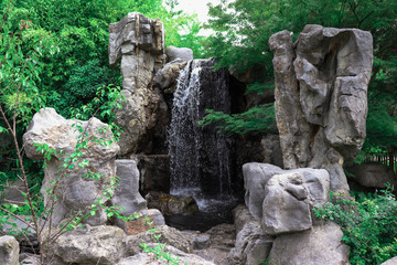 Amazing view of falling waterfall among rocks in a garden.