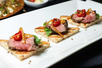 Slices of steak, with sun-dried tomato and Dijon mustard, laid out on toast.