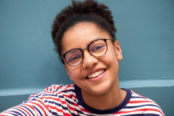 Close up of smiling young black girl with glasses against blue wall