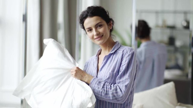 Beautiful young woman at home sitting in bed holding a pillow in her hands.