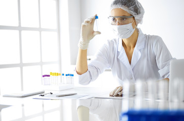 Professional female scientist in protective eyeglasses researching tube with reagents in laboratory. Concepts of medicine and research