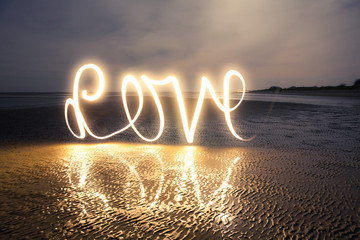 Light Painting Art: Writing love with light into darkness on the beach at a romantic twilight - obrazy, fototapety, plakaty