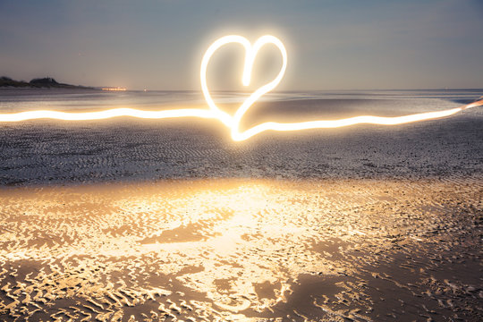 Romantic light painting : Heart drawn with flashlight at blue hour on the beach near the water at low tide