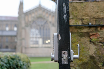 Shallow focus of an opened park door showing a digital type, combination lock, allowing members of the public access to a large Cathedral seen out of focus in the background.