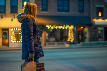 woman standing along city street holding Christmas shopping bags at night