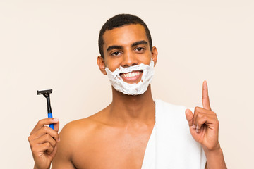 Young handsome man shaving his beard over isolated background pointing up a great idea