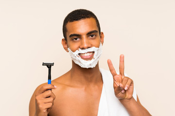 Young handsome man shaving his beard over isolated background smiling and showing victory sign