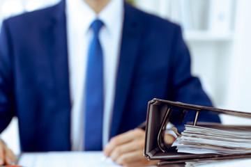 Binders with papers waiting to be processed with businessman or bookkeeper back in blur. Accounting...
