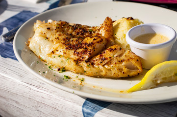 Delicious Cod Fillet with Seasonings on Top, Lemon and Sauce on Side. Authentic Shot from an Irish Seafood Restaurant.
