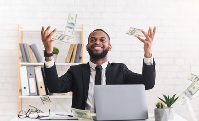 Happy young businessman in suit throwing money up at workplace