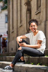 Obraz premium happy young african american girl sitting outside in city with cellphone