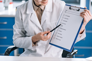 cropped view of happy woman holding pen near clipboard with checklist