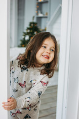 Little happy brunette girl in cozy pajamas looks from children bed room, christmas time