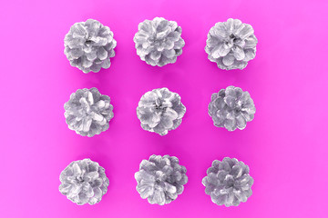 Christmas pattern. Flat lay square made with many silver cones in the centre on the pink background. Top view.