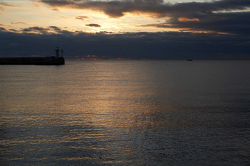 Naklejka na ściany i meble Pier with a small lighthouse on the background of the pre-dawn sky.