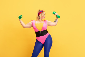Young caucasian plus size female model's training on yellow background. Copyspace. Concept of sport, healthy lifestyle, body positive, fashion, style. Stylish woman practicing with green weights.