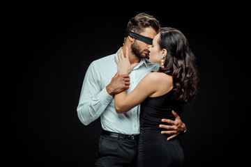 sexy woman touching blindfolded man isolated on black