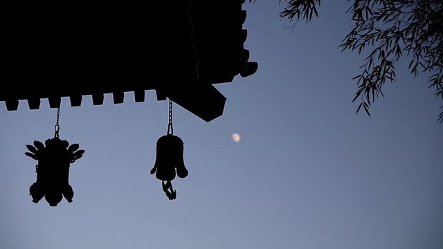 Lanterns hanging from temple roof with moon in the night sky