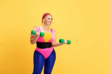 Fototapeta premium Young caucasian plus size female model's training on yellow background. Copyspace. Concept of sport, healthy lifestyle, body positive, fashion, style. Stylish woman practicing with green weights.