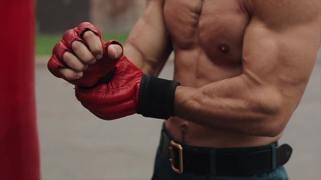 Close view of shirtless muscular man wrapping hand with black boxing bandage